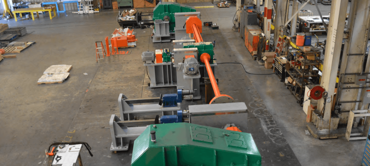 Orange and green span drive machinery seen from above in a fabrication shop.