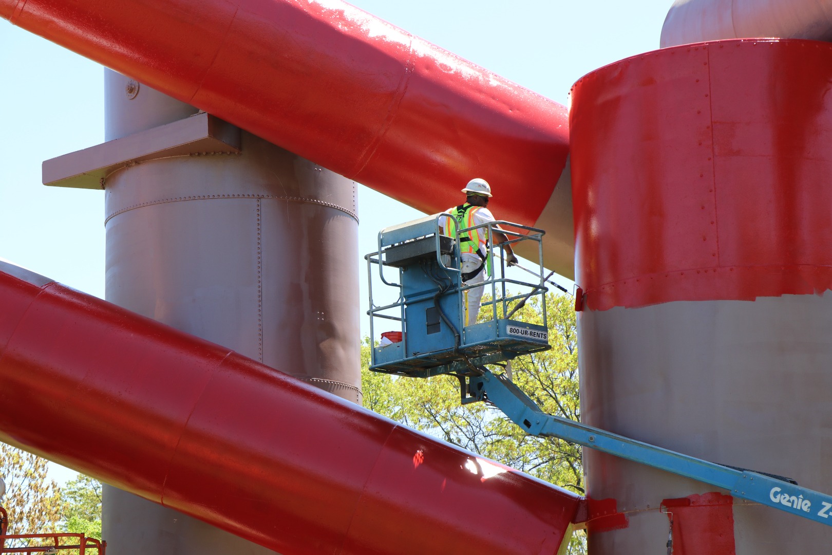 Painters apply a bright red topcoat to a large sculpture made of reclaimed steel tanks.